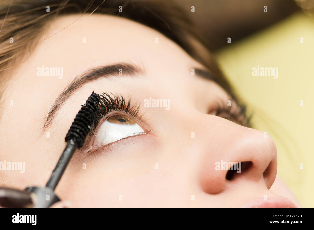 Closeup headshot brunette getting makeup treatment by professional stylist applying mascara on eyelashes Stock Photo