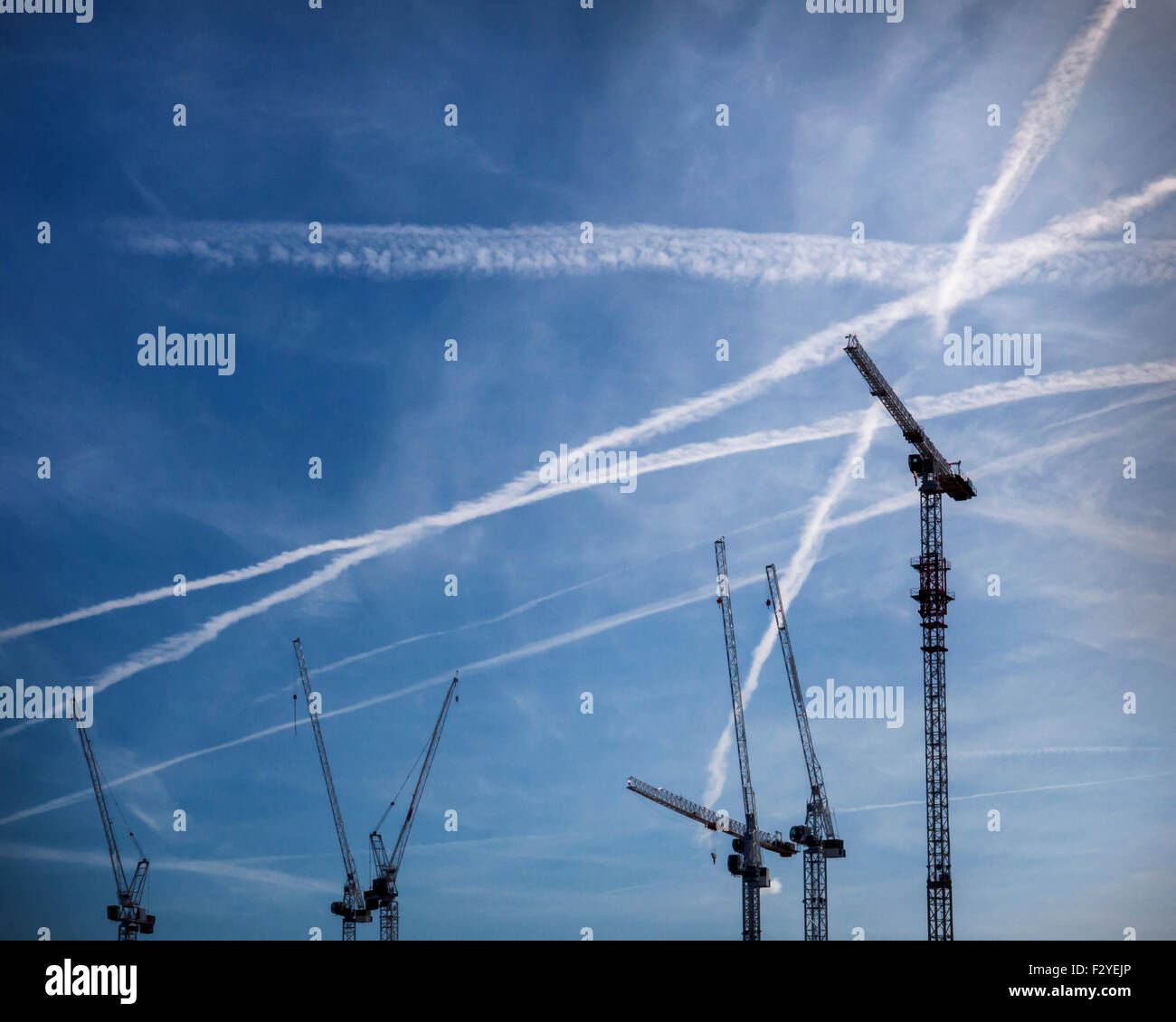 Cranes and planes condensation trails, contrails. urban landscape with dramatic blue sky, Greenwich, London Stock Photo