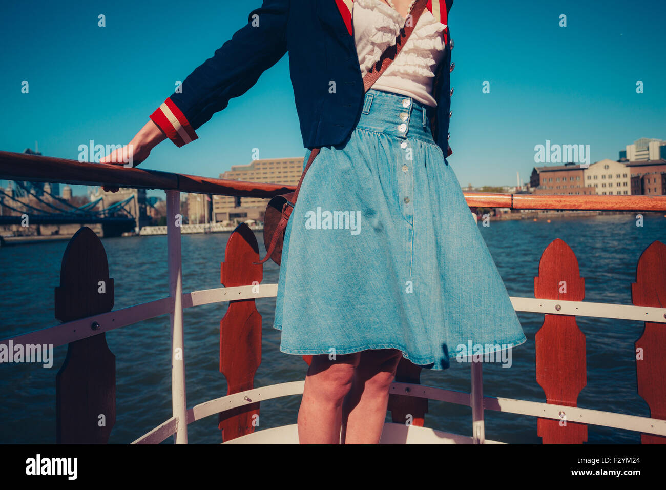 A young woman's skirt is blowing in the wind as she is standing on the deck of a boat cruising down the river Stock Photo