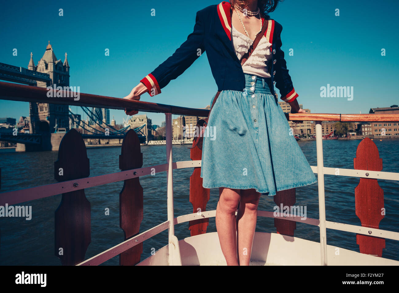 A young woman's skirt is blowing in the wind as she is standing on the deck of a boat cruising down the river Stock Photo