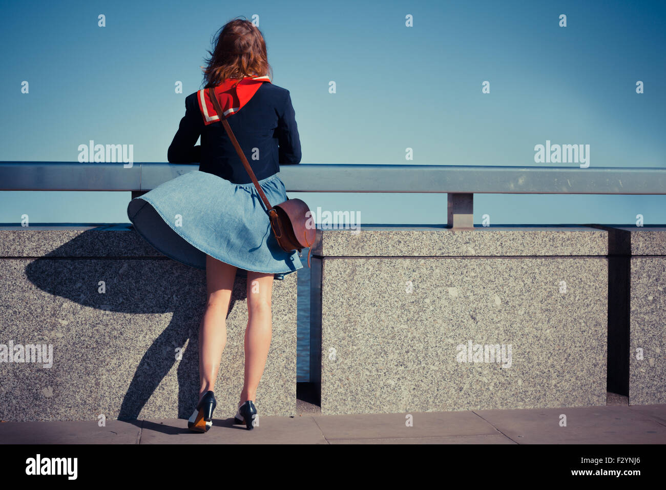 A young woman is standing on a bridge with her skirt blowing in the wind Stock Photo