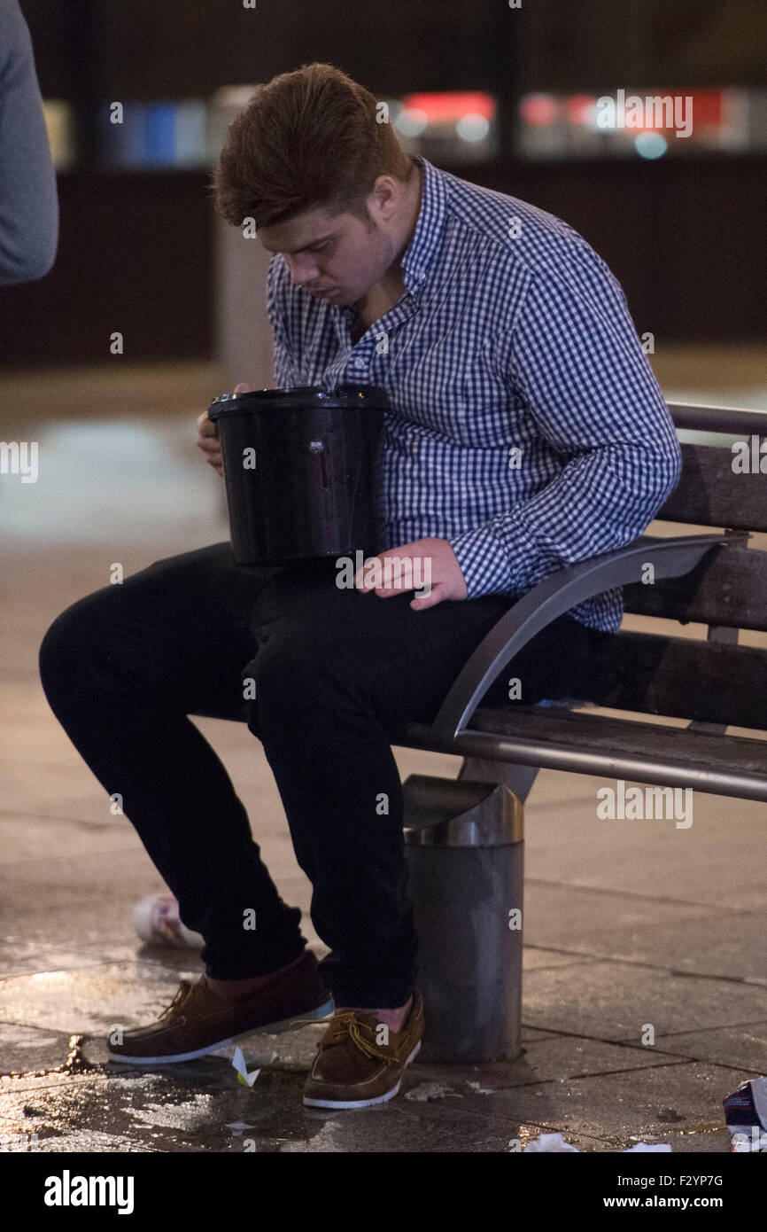 A man is sick into a bucket in Cardiff, South Wales. Stock Photo
