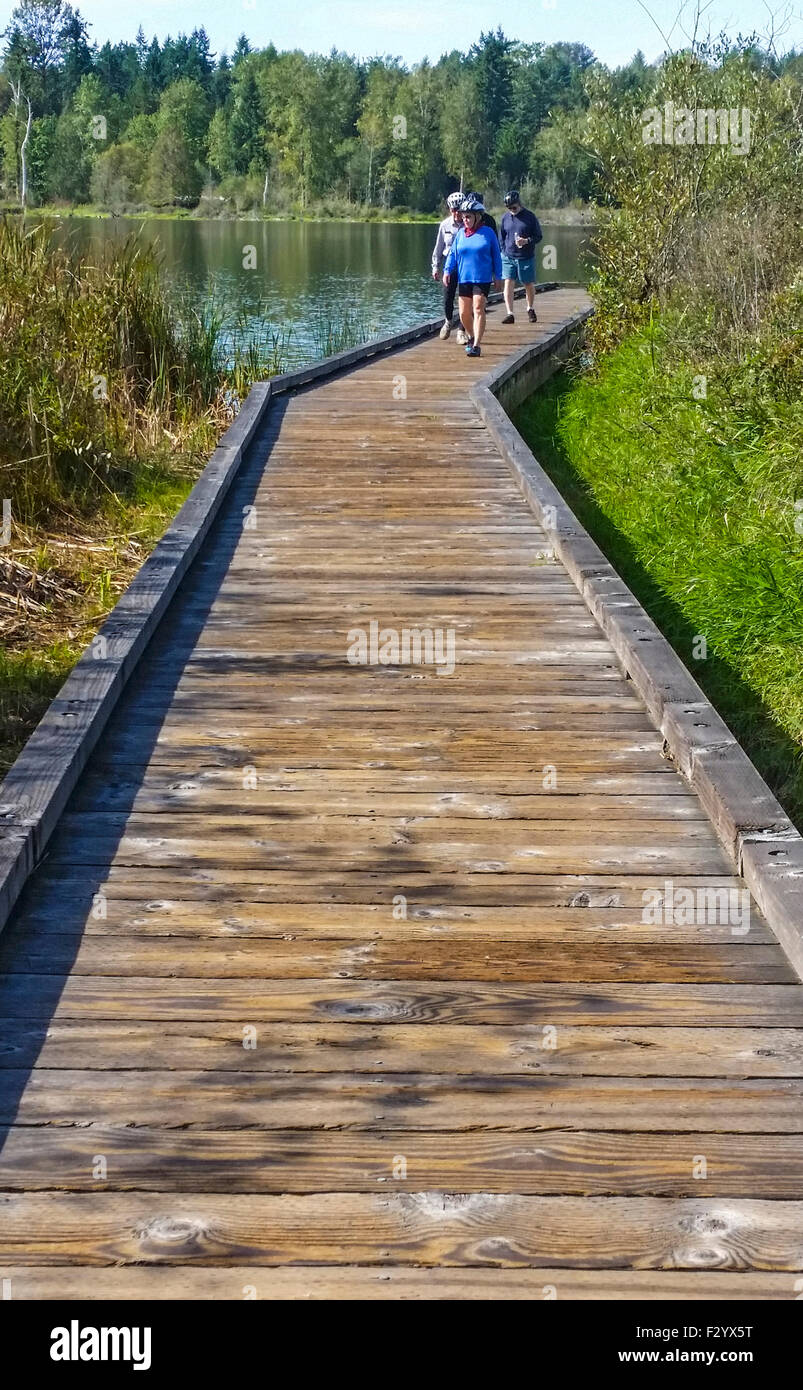 Bicyclists walk down wooden dock after viewing Lake Cassidy along the