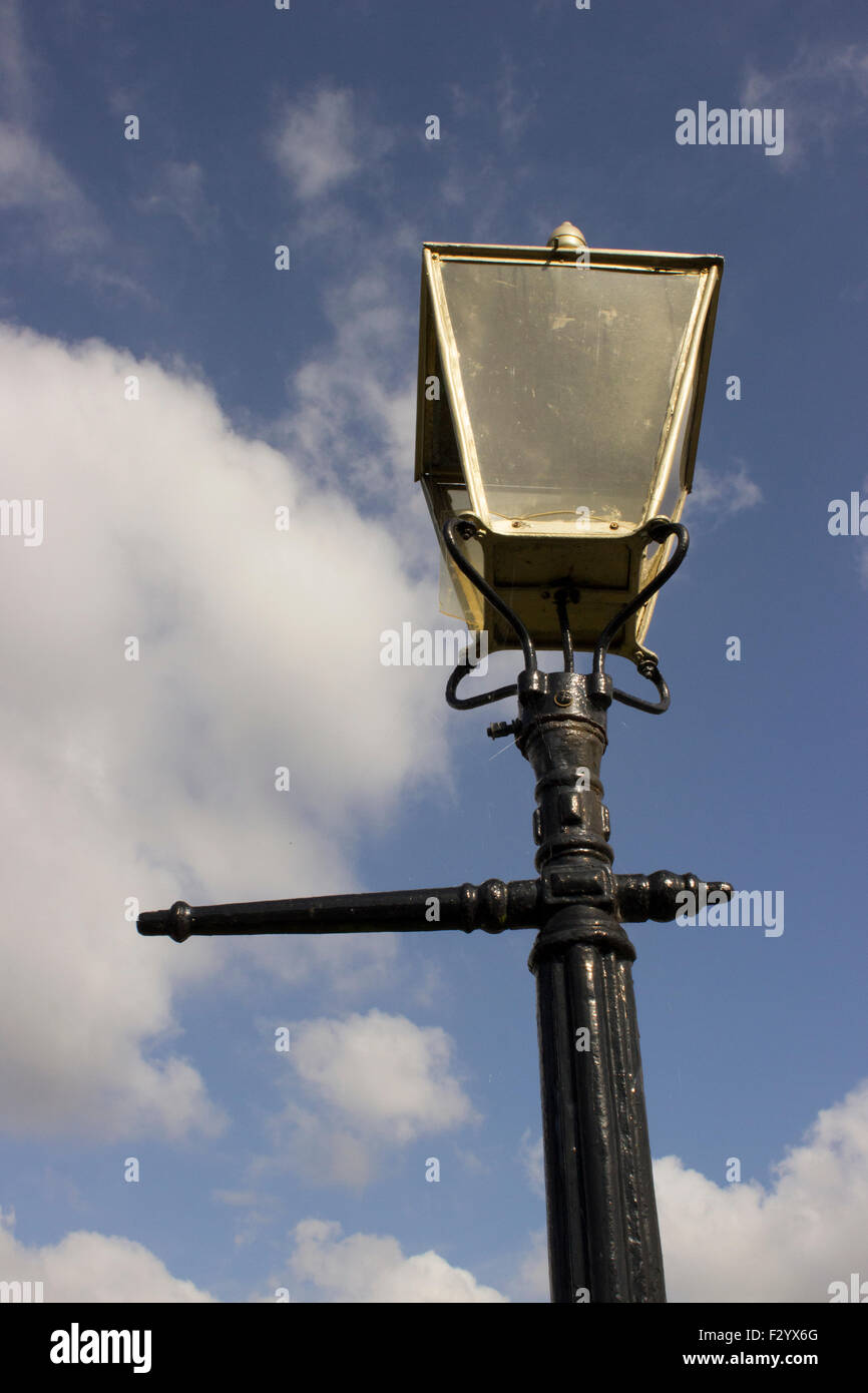 Old style gas burning streetlamp, lantern, with a black post and a gold head. its a blue sky behind with a few clouds. Stock Photo