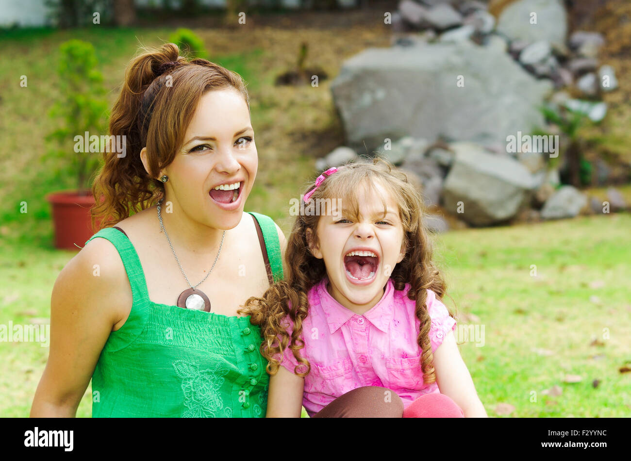 Mother and daughter sitting outside in park environment laughing, enjoying Stock Photo