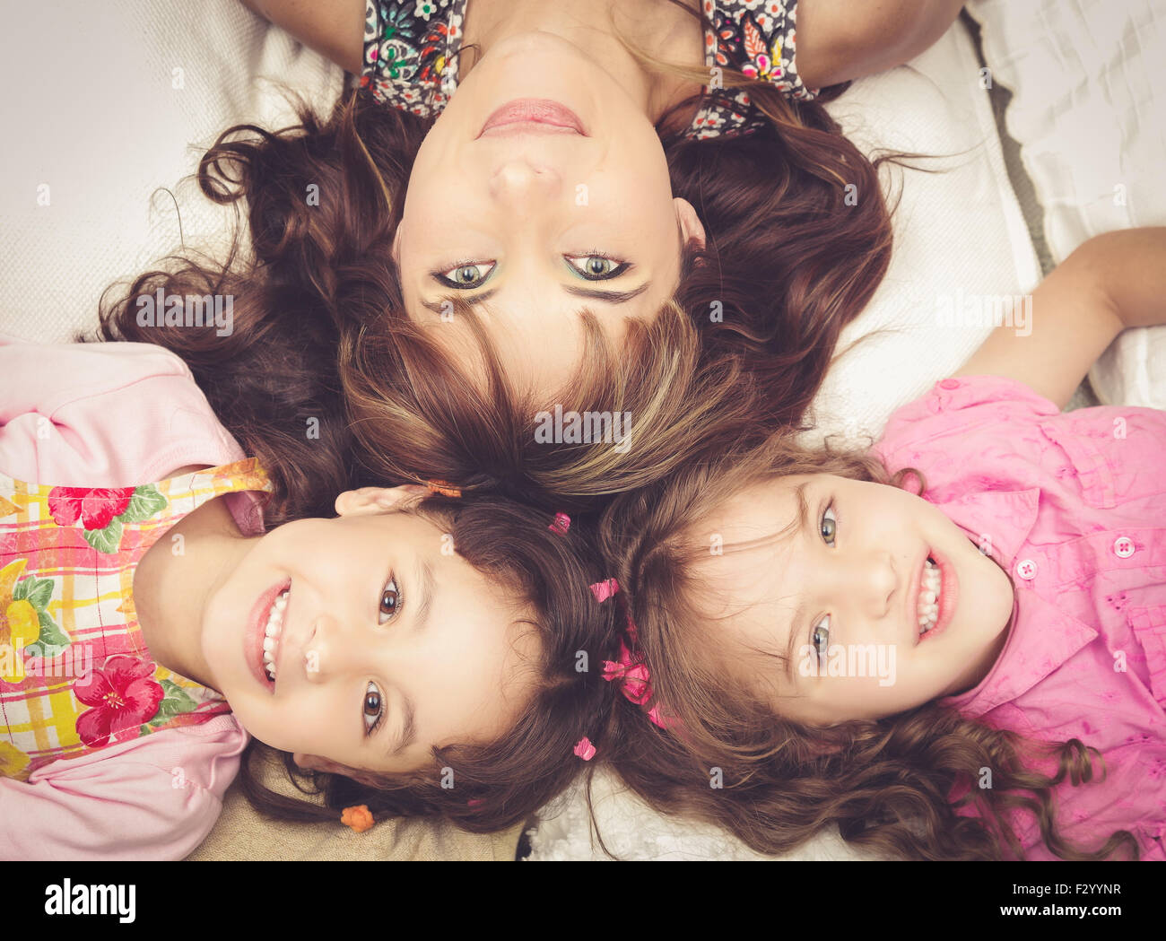 Young adorable hispanic sisters and mother lying down with heads touching, bodies spread out different directions closeup Stock Photo