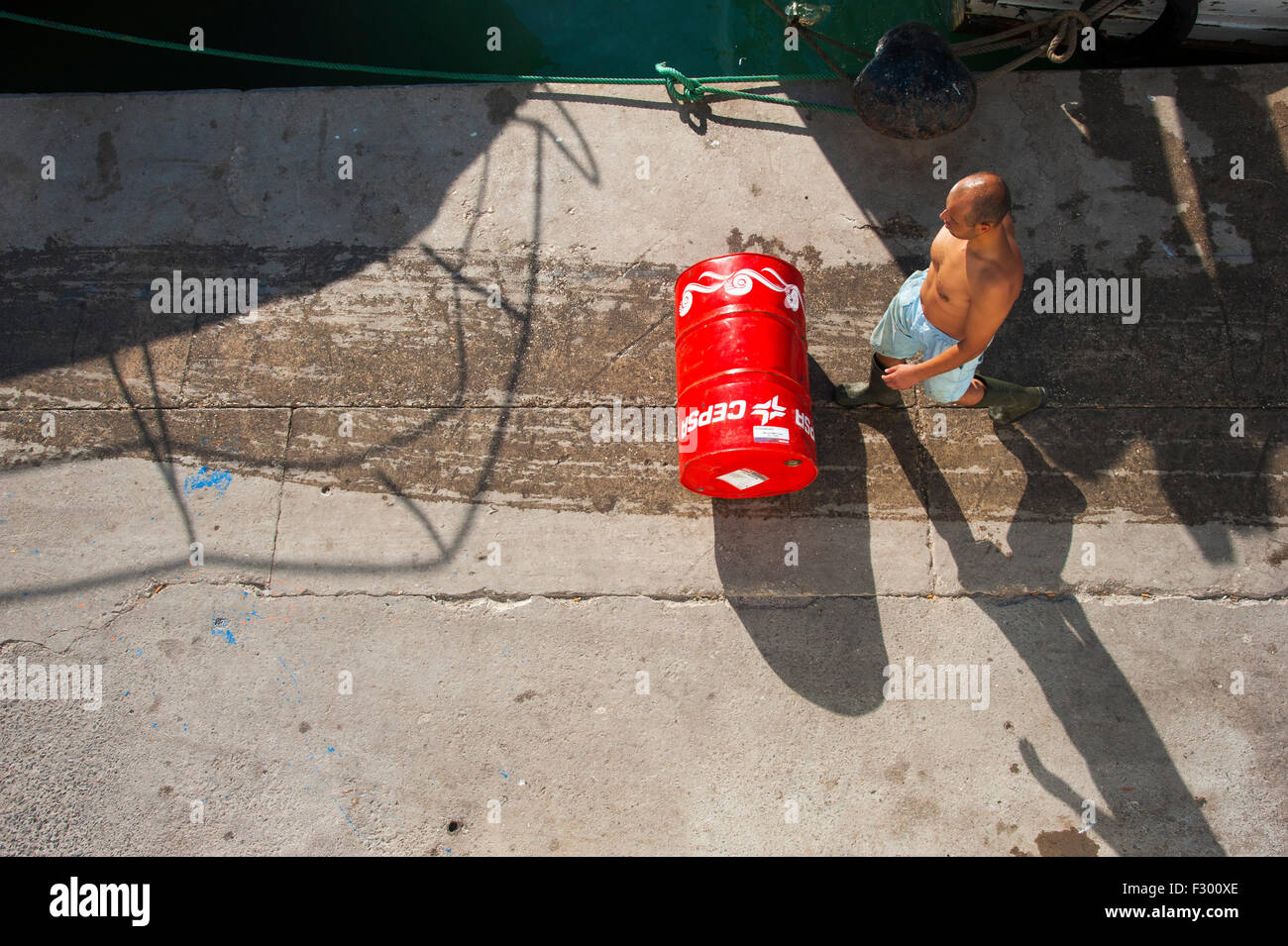Sailor rolling a red barrel with oil brand Cepsa on the quay of the fishing port of Altea, Alicante, Costa Blanca, Spain Stock Photo