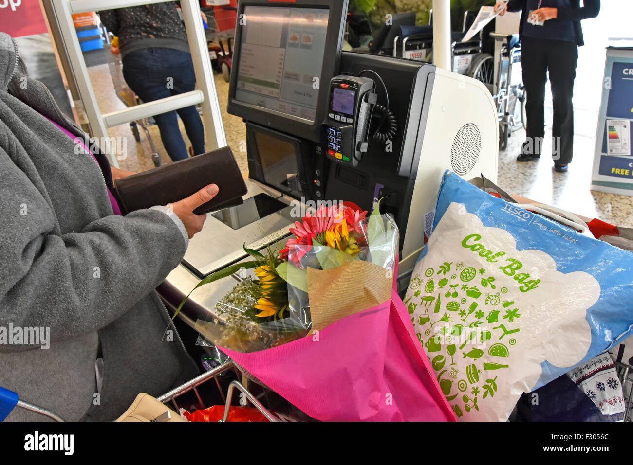 Woman shopping Tesco self service checkout scan as you shop till download data from hand held scanner beside full weekly food shop trolley England UK Stock Photo