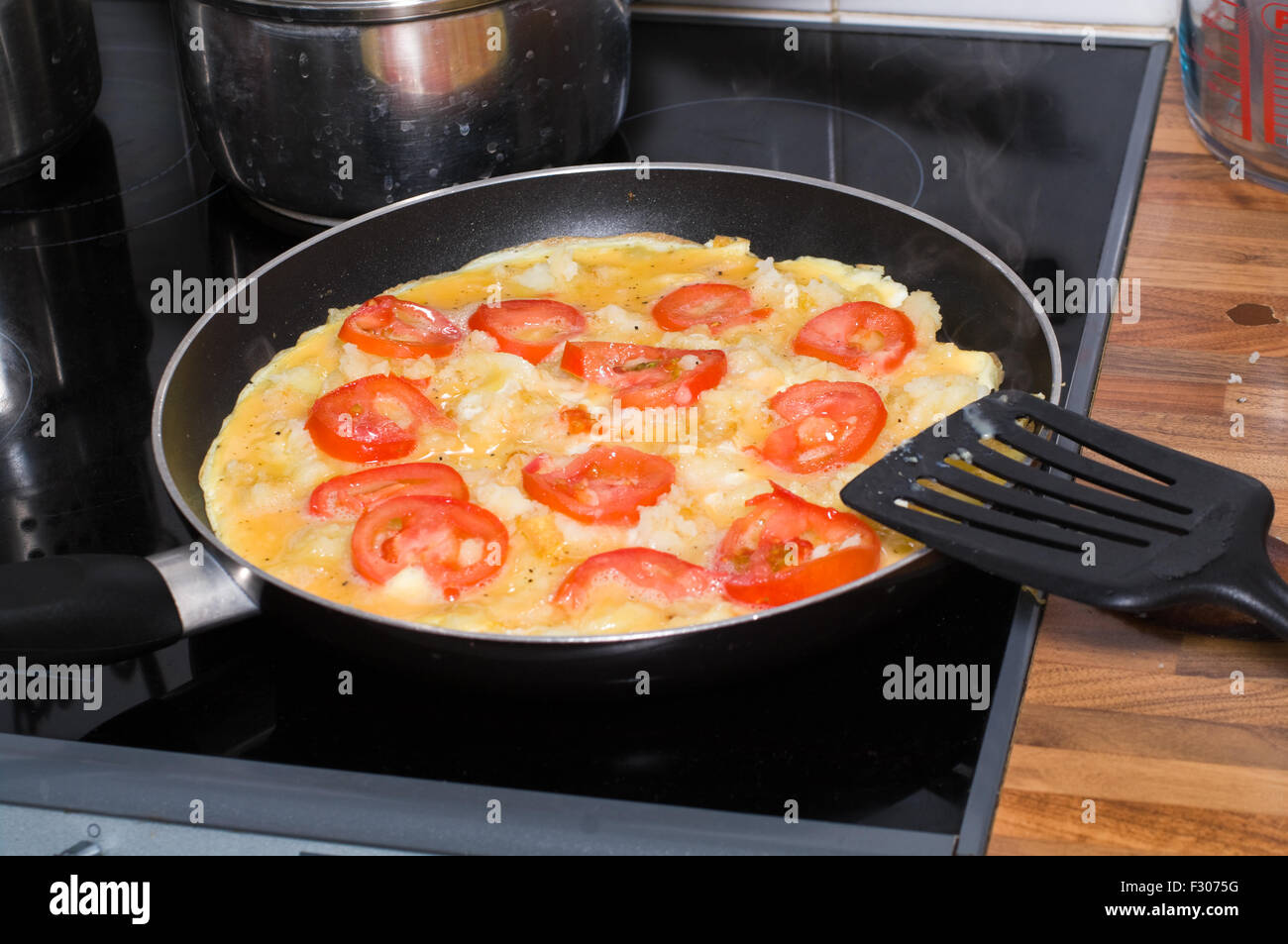 Spanish omelette with tomatoes being cooked in a frying pan. Stock Photo