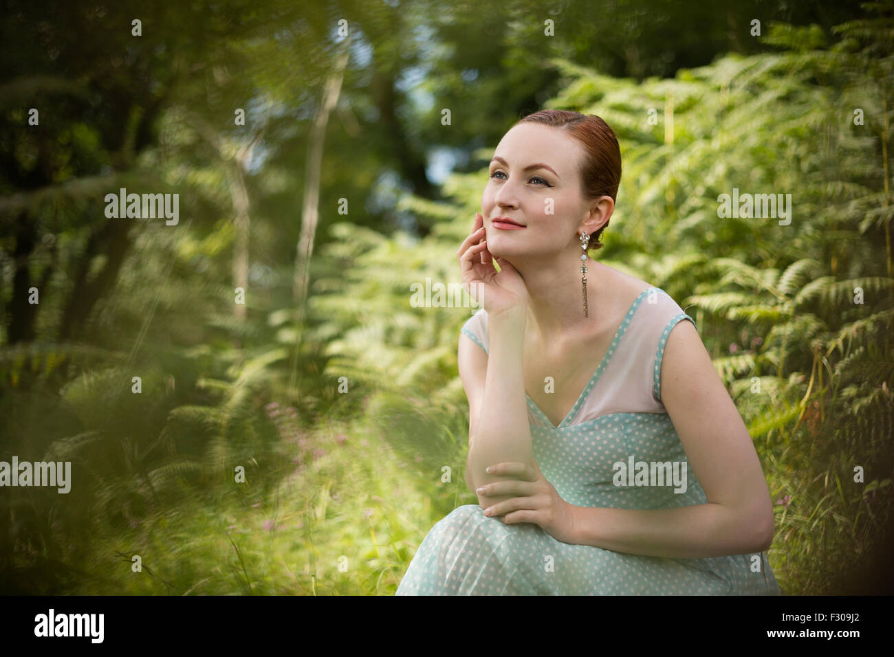 Woman in a summer dress, sitting in front of ferns in Cheddar Gorge. Stock Photo