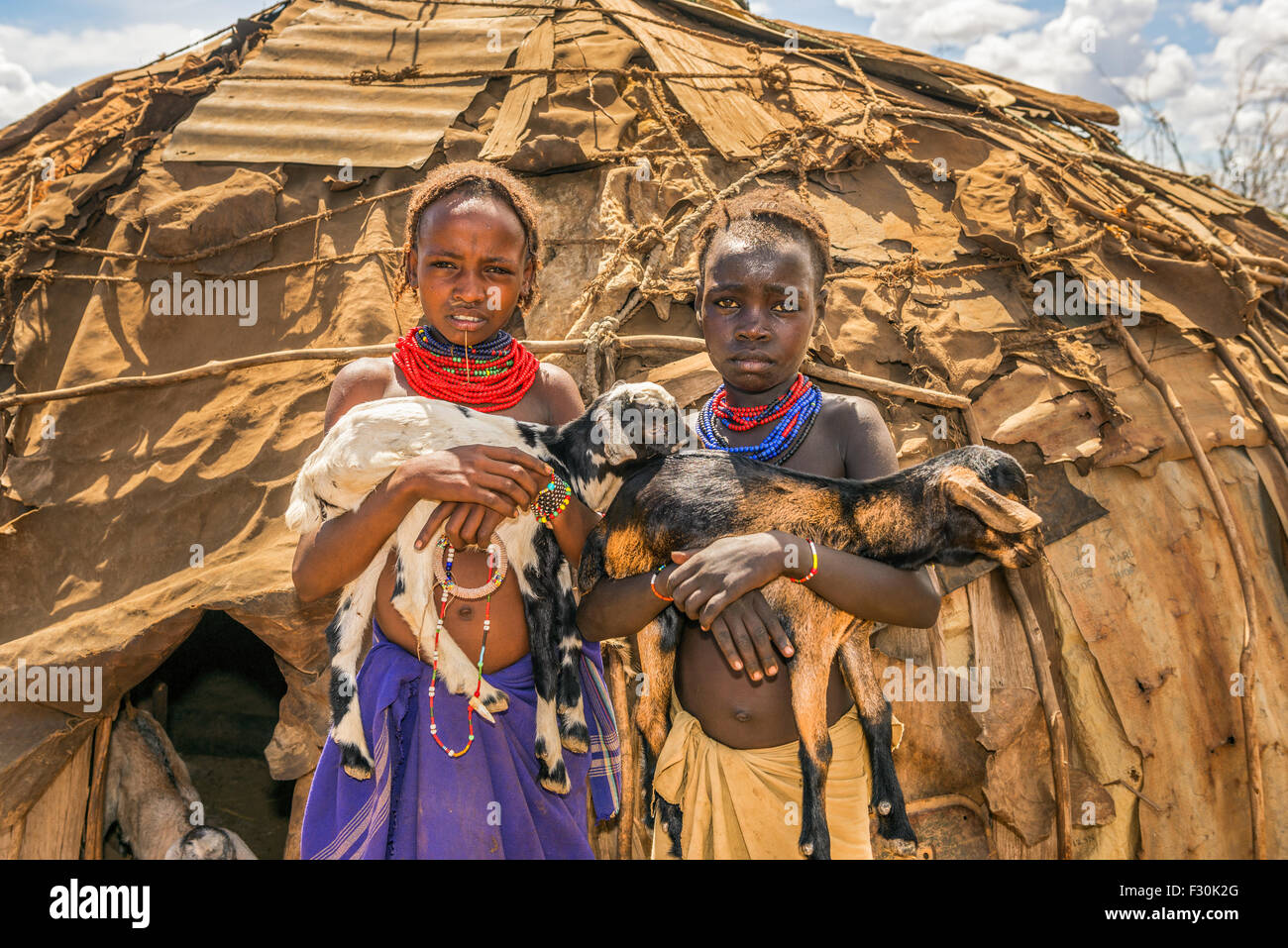 Two girls from the African tribe Daasanach holding goats in front of their home. Stock Photo