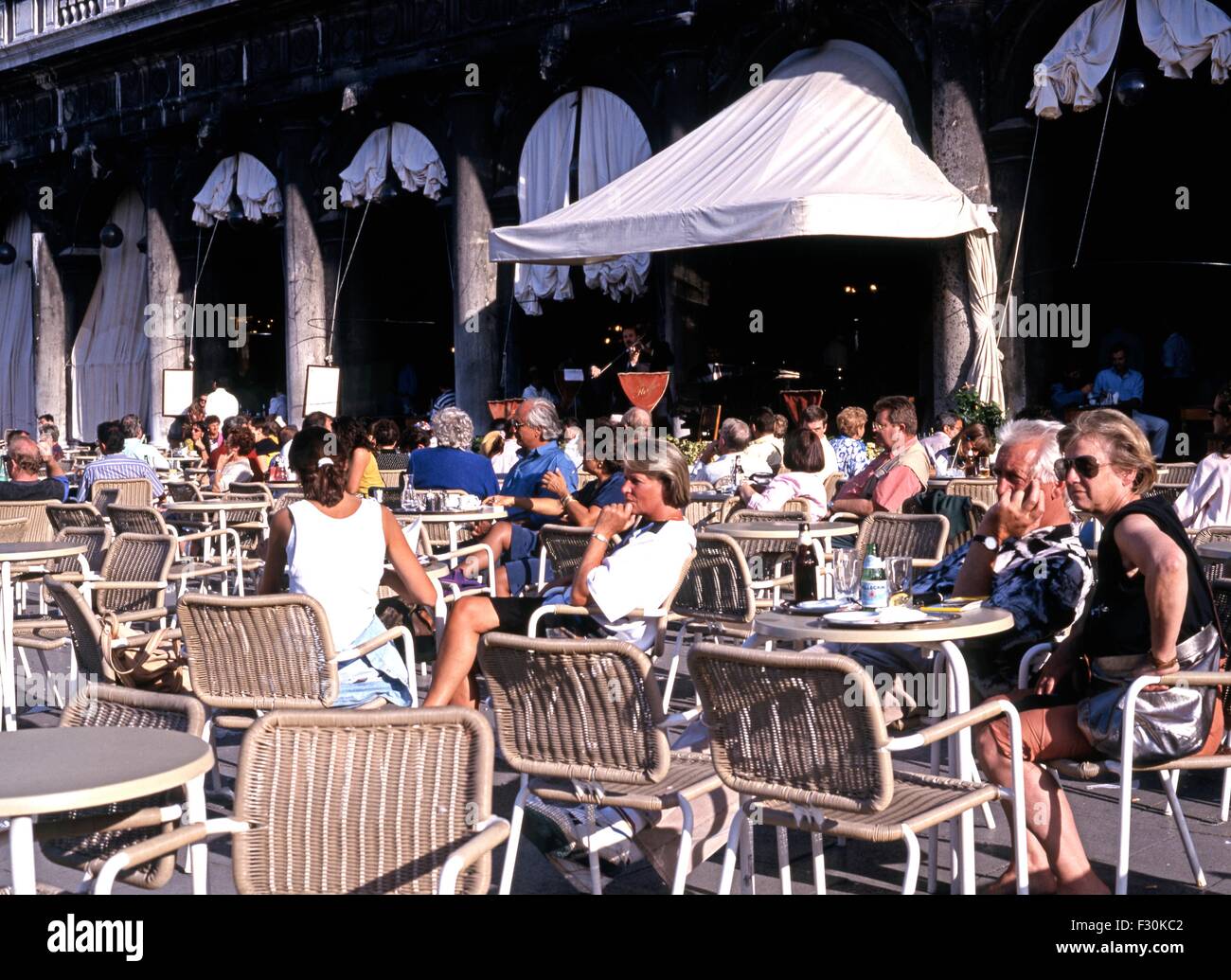 Tourists at a pavement cafe with musicians to the rear in St Marks Square, Venice, Veneto, Italy, Europe. Stock Photo
