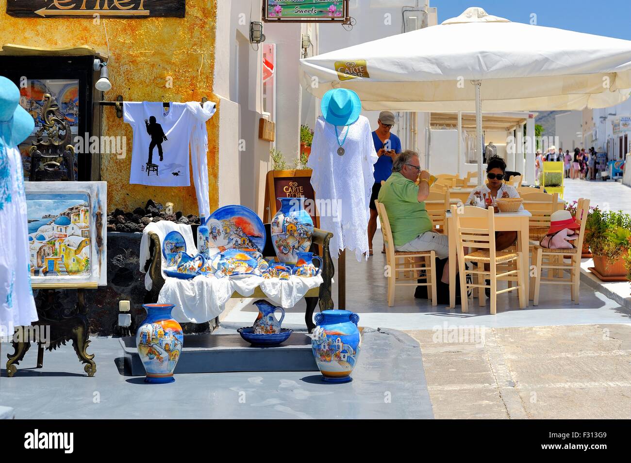 Tourists enjoying a drink outside a street cafe next to a souvenir shop in the village of Oia Santorini greece Stock Photo