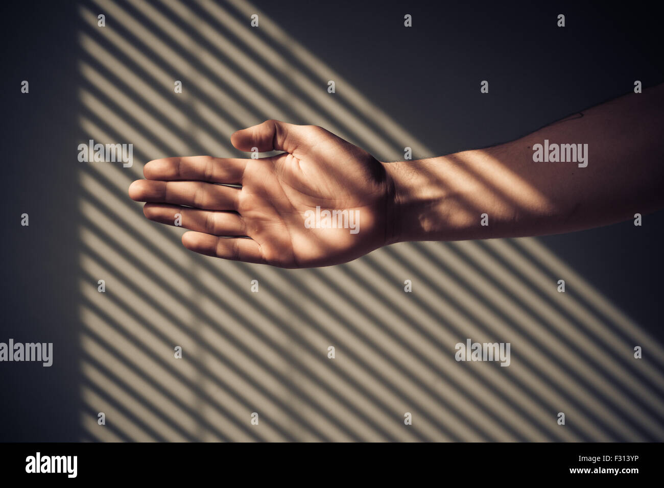 Man's hand with shadows being cast from blinds Stock Photo
