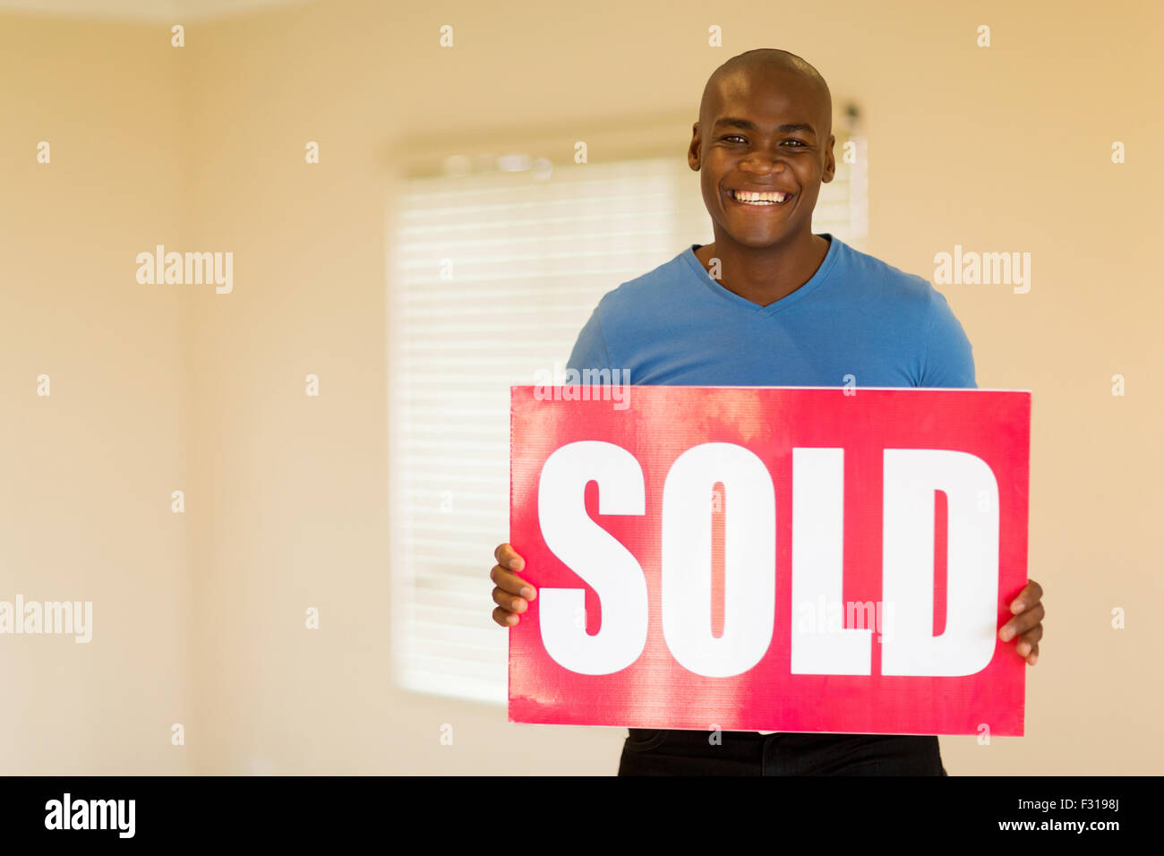 happy young black man holding sold sign in his home Stock Photo