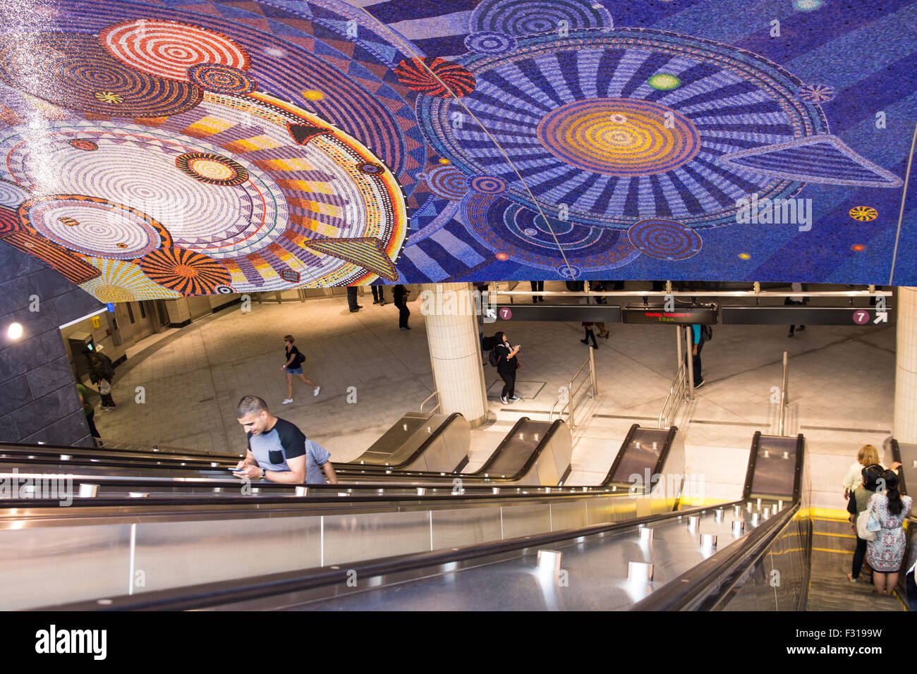 View escalator and mosaic tile ceiling at new Hudson Yards 7 train subway station with travelers visible. Stock Photo