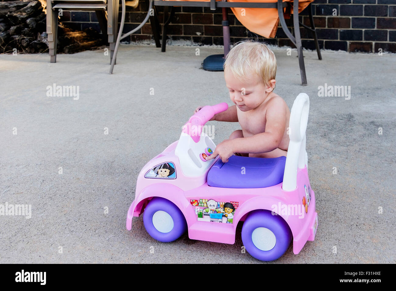 A one year old Caucasian baby girl plays with her riding toy car. USA Stock Photo