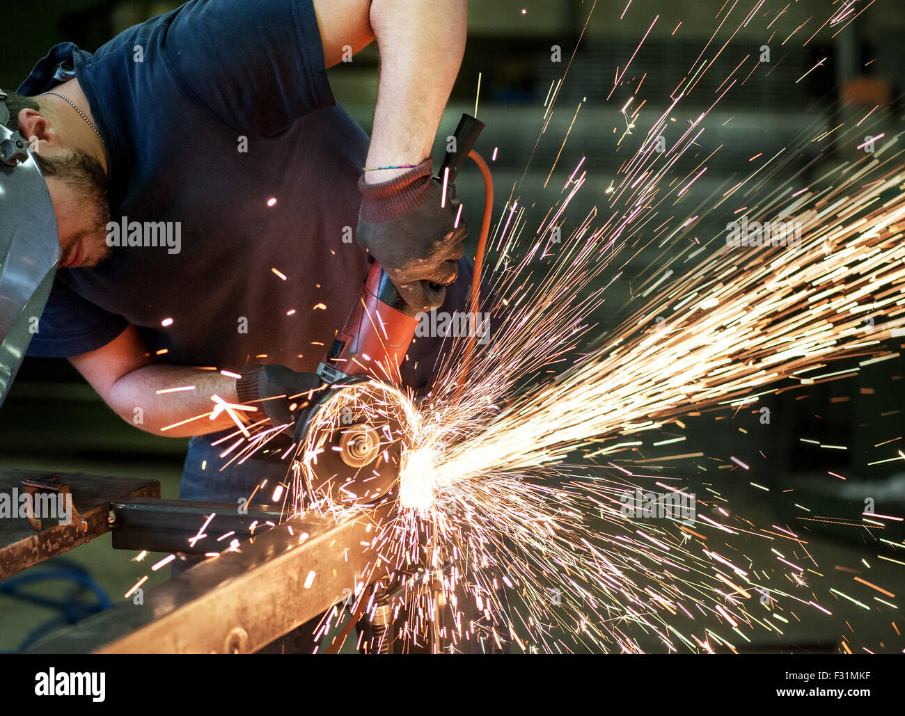 Metalworker cutting a steel bar using a hand held angle grinder power