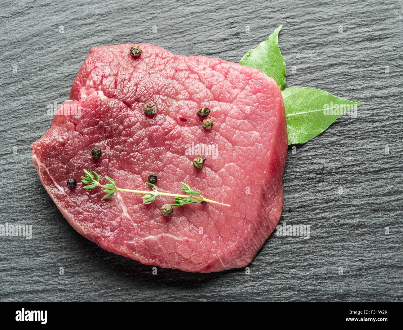 Raw beef steaks with spices on the black cutting board. Stock Photo