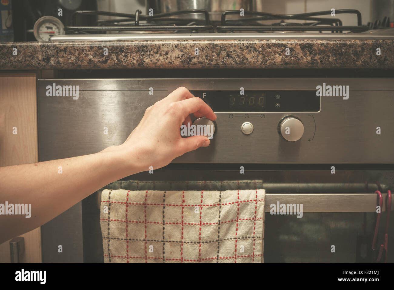 The hand of a young woman is turning the knob on a stove Stock Photo