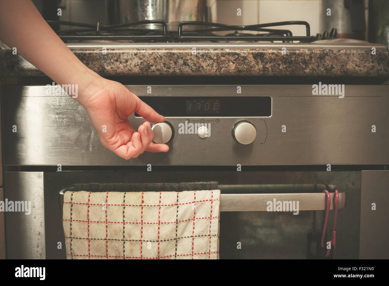 The hand of a young woman is turning the knob on a stove Stock Photo