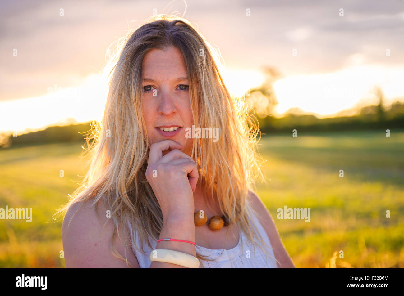 A strong backlit portrait of a woman (aged 25 - 30) in a field on a summers evening Stock Photo