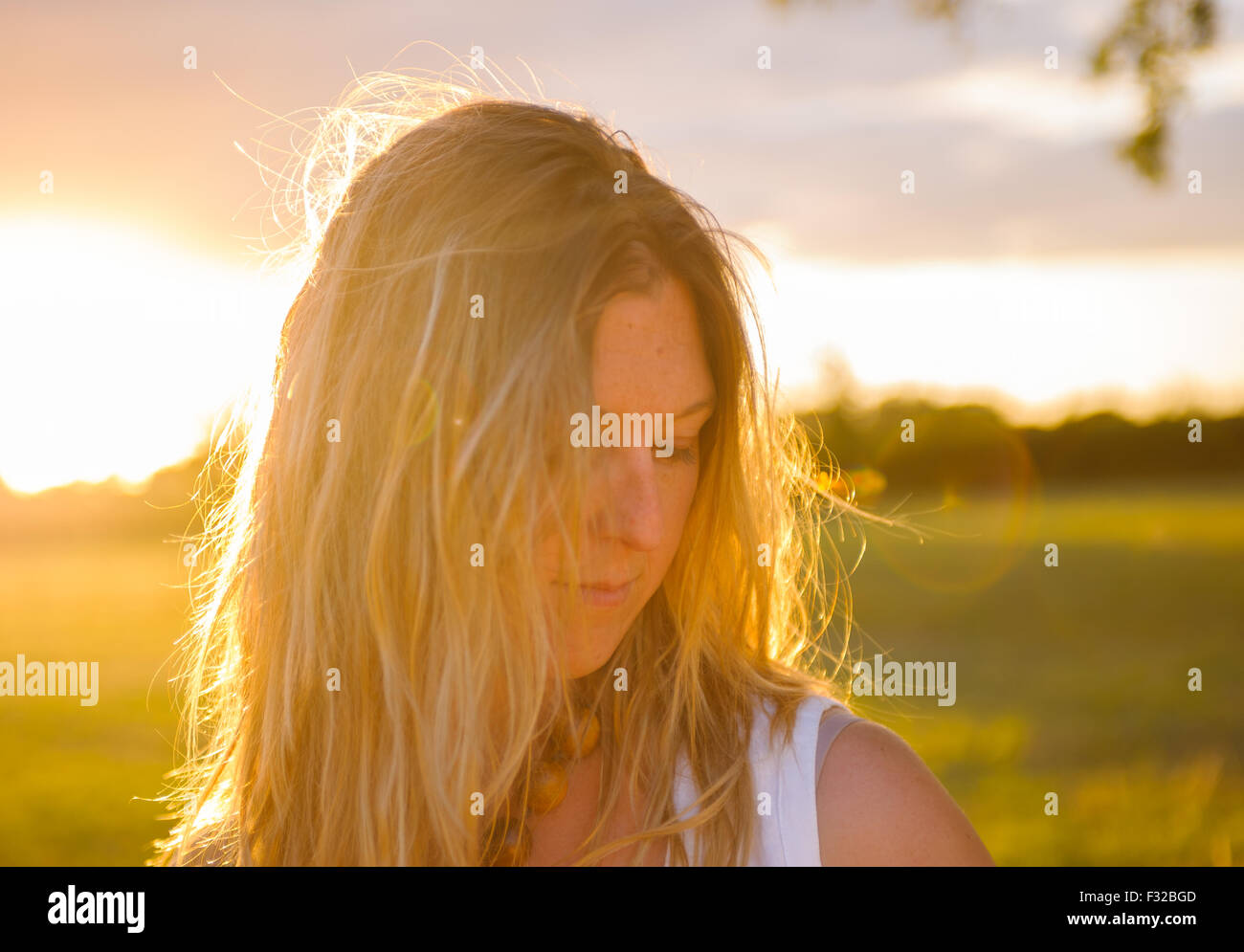 A strong backlit portrait of a woman (aged 25 - 30) in a field on a summers evening Stock Photo