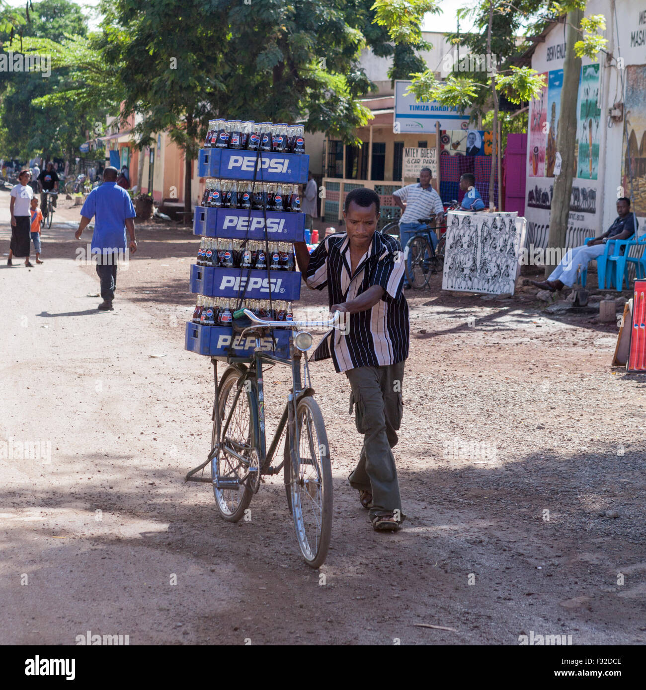 Man wheeling bicycle load of Pepsi on dirt street , Mto Wa Mbu, Tanzania. This village is on the main Arusha to Serengeti road. Stock Photo