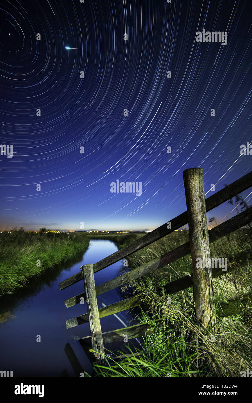 View of cattle fencing, water-filled ditch and star trails on coastal grazing marsh habitat at night, Elmley Marshes N.N.R., North Kent Marshes, Isle of Sheppey, Kent, England, July Stock Photo