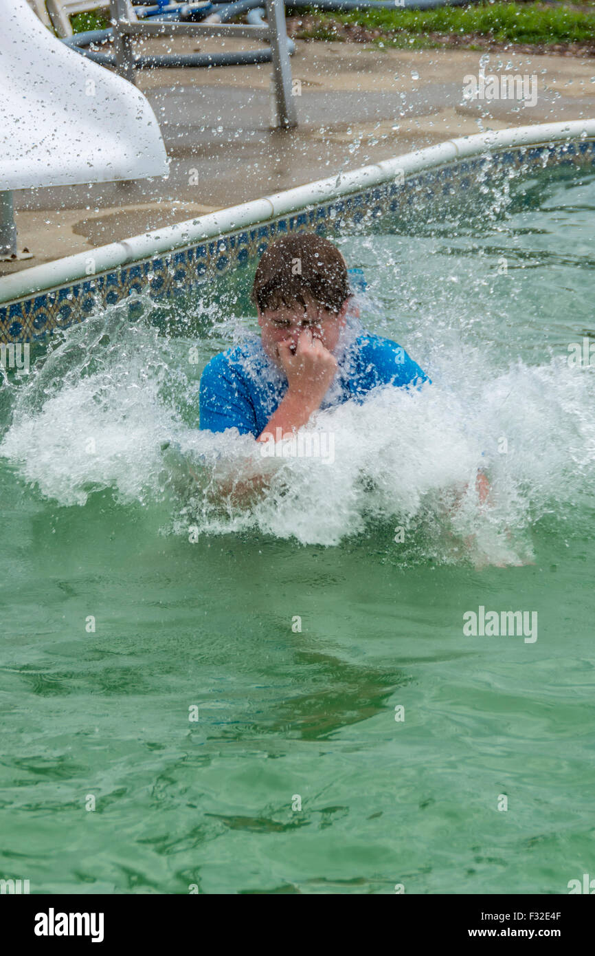 Teenage boy holding his nose while he jumps into a swimming pool Stock Photo