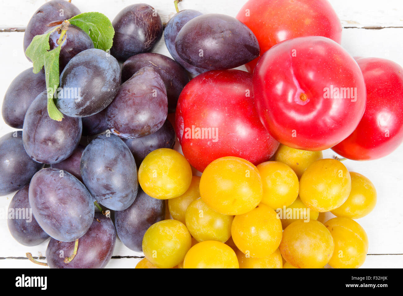 three varieties of plums on a white wooden table Stock Photo - Alamy