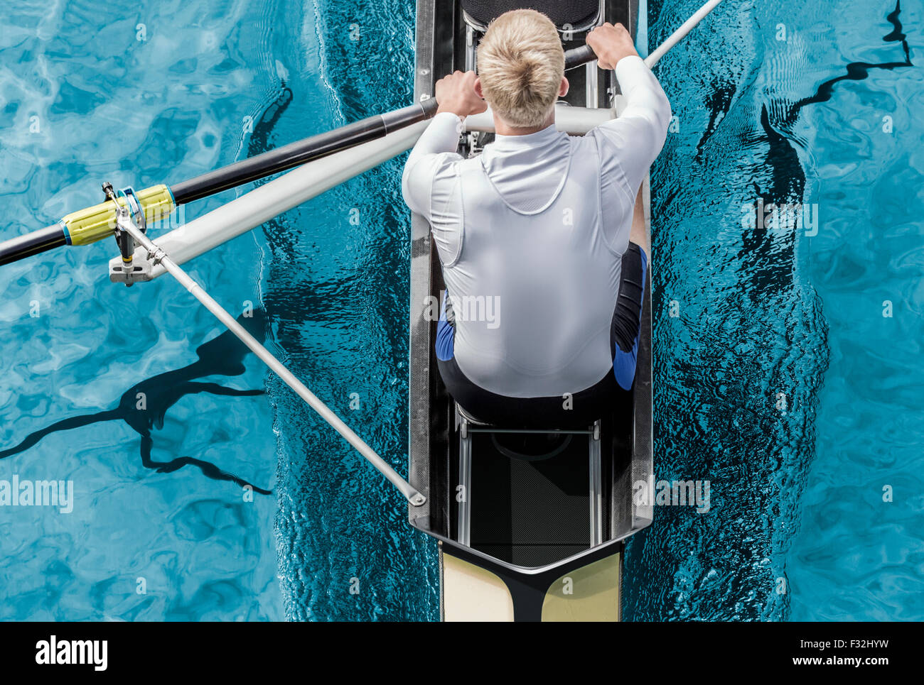 Top view of athletic competition rower, who strokes his  paddle through metallic blue water. Stock Photo
