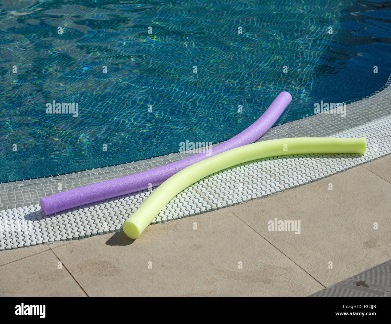 Two water aerobics noodles of bright colors are in sunlight on the edge of swimming pool. Stock Photo