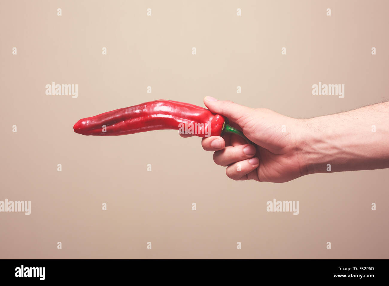 A man's hand is holding a red pepper like a gun Stock Photo