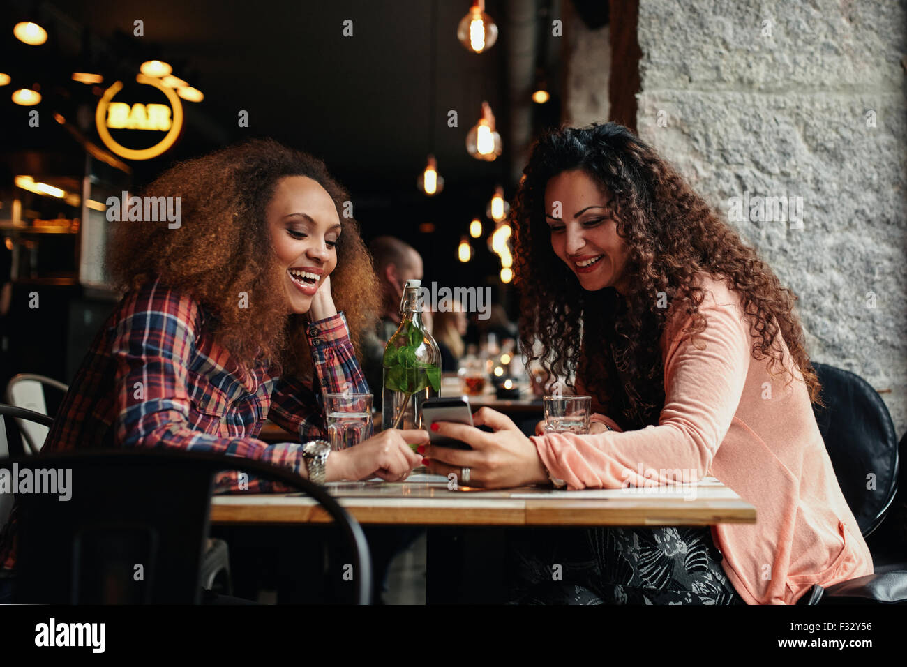 Young women sitting at cafe and using phone. Friends sitting in a restaurant with one woman showing something interesting to her Stock Photo