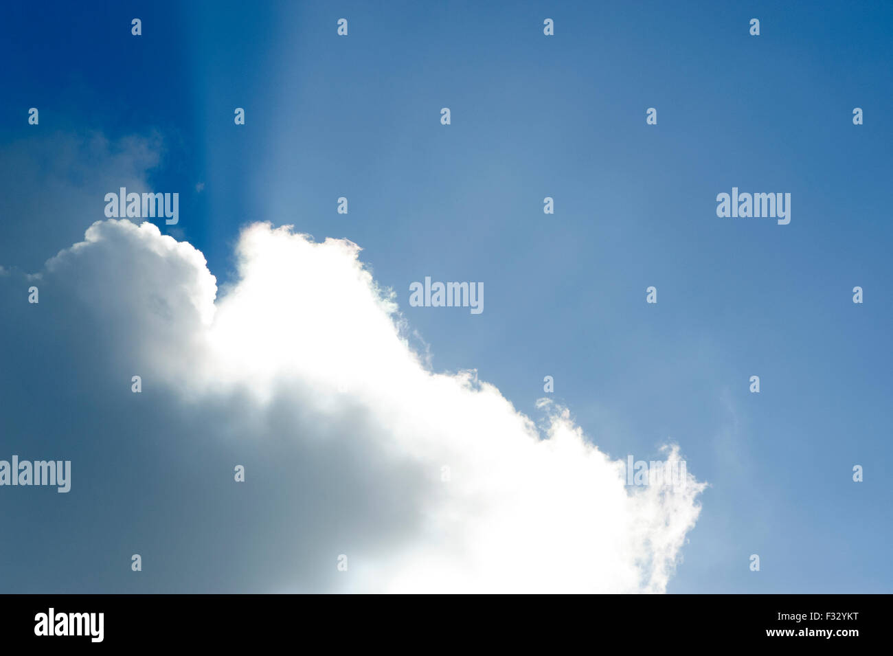 large cloud against blue sky with shafts of sunlight shining from behind Stock Photo