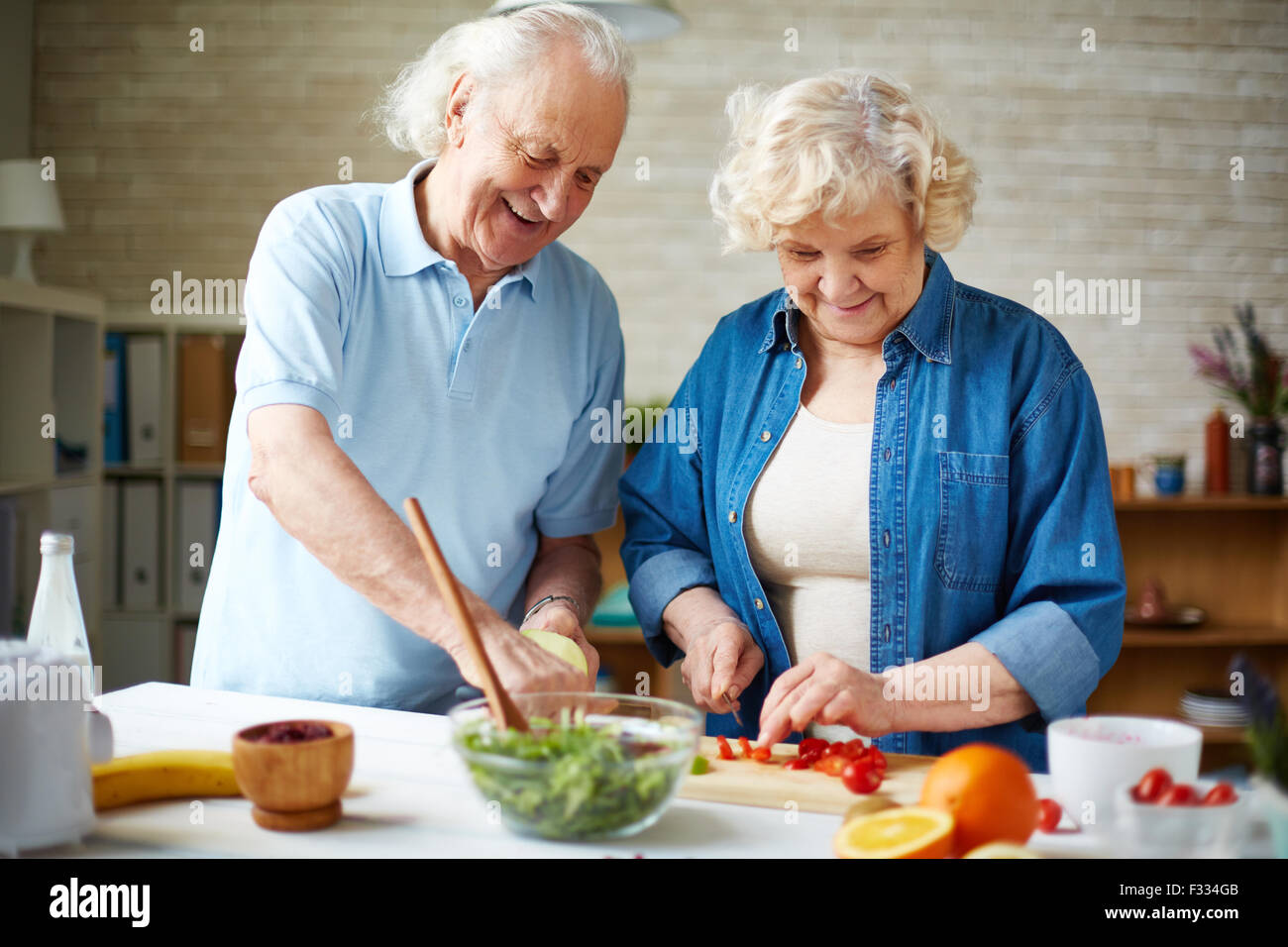 Happy senior couple preparing fresh vegetable salad in the kitchen Stock Photo