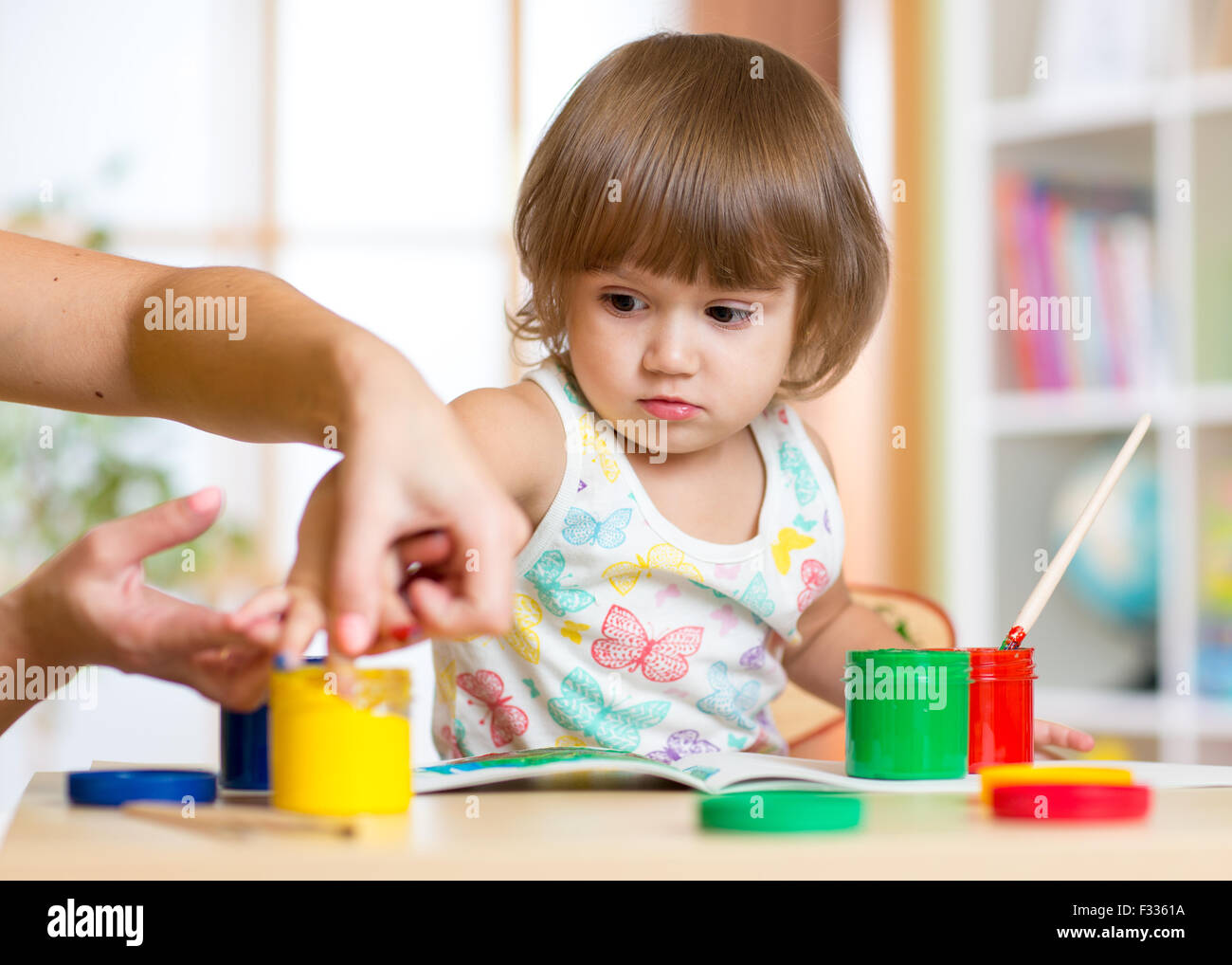 Teacher and child painting together at nursery with paintbrushes and watercolors Stock Photo