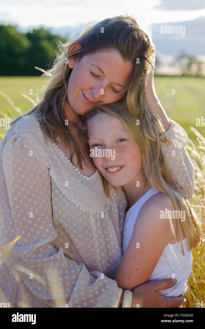 A backlit portrait of a woman (aged 25 - 30) with her daughter (aged 8) sat in in a field of long grass on a summers evening Stock Photo