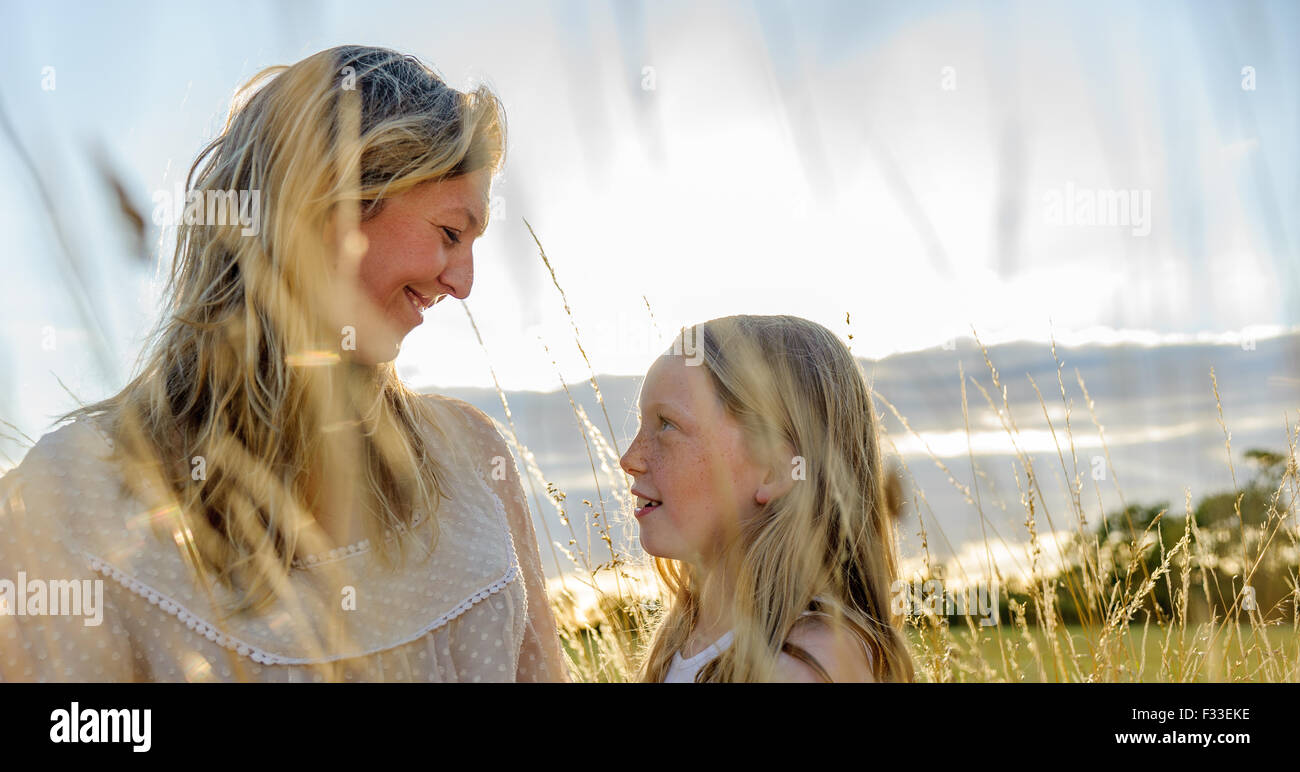 A backlit portrait of a woman (aged 25 - 30) with her daughter (aged 8) sat in in a field of long grass on a summers evening Stock Photo