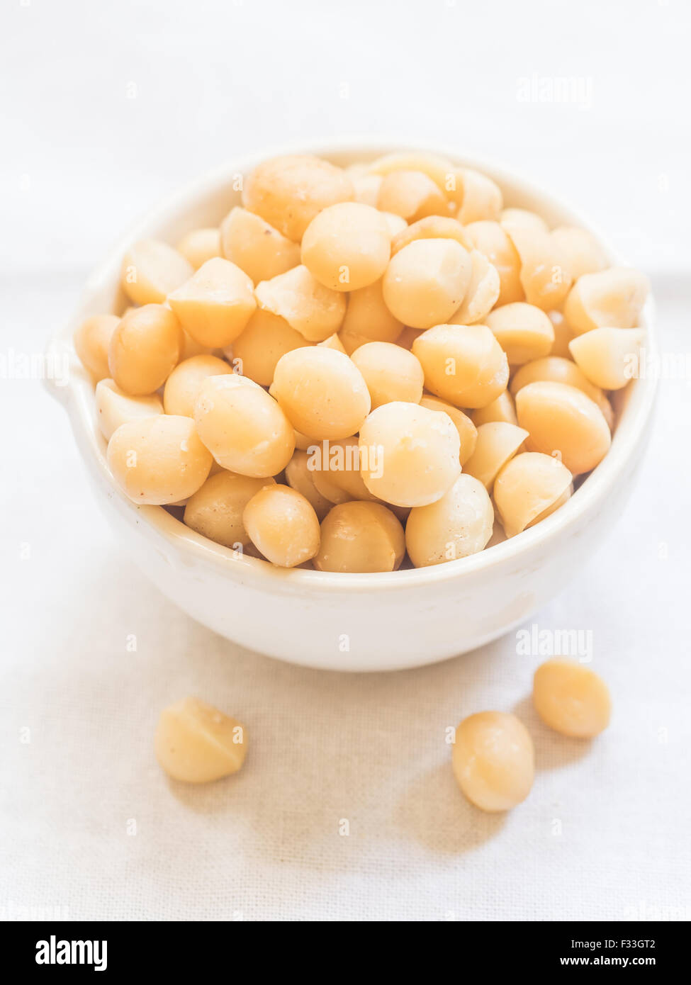 Macadamia nut in a white bowl, on a clear white background. Stock Photo