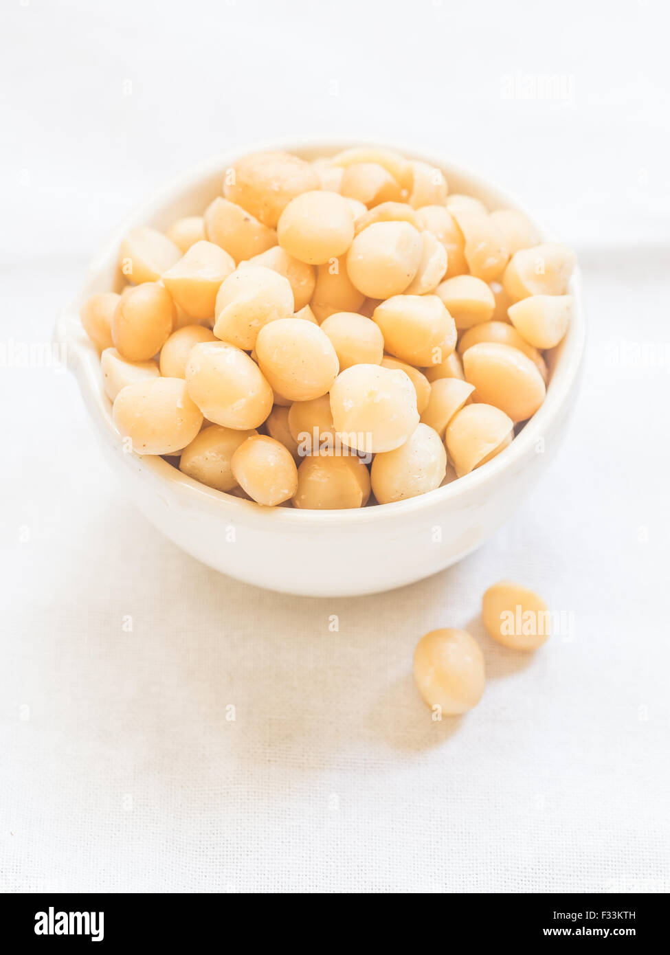 Macadamia nut in a white bowl, on a clear white background. Stock Photo