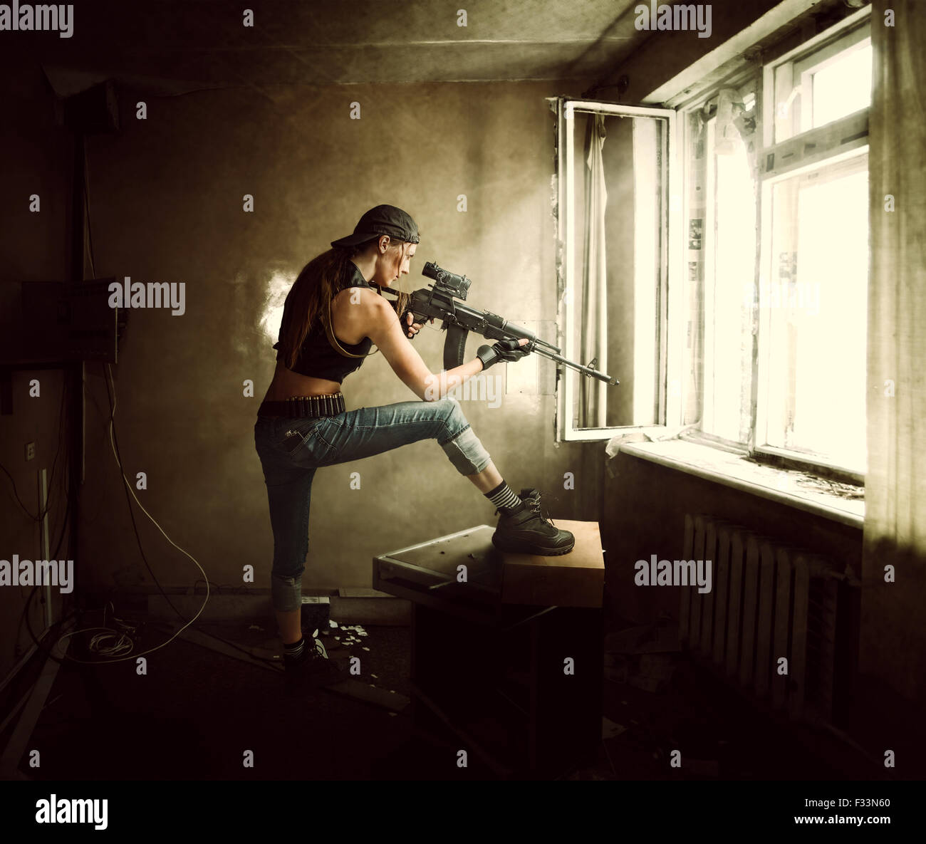 Young beautiful woman sniper and Soldier aiming a rifle at the window. She is in old room of abandoned building Stock Photo