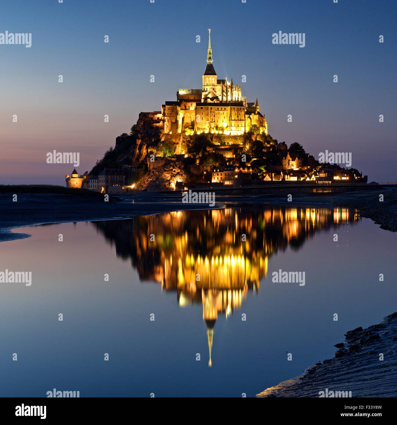 A colour image of reflections of Mont Saint Michel lit up at dusk in a water pool on the beach at Mont Saint Michel Stock Photo