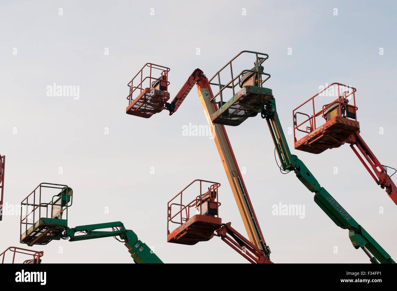 Boom lifted  empty cherry picker cages set against a sunset sky. Stock Photo