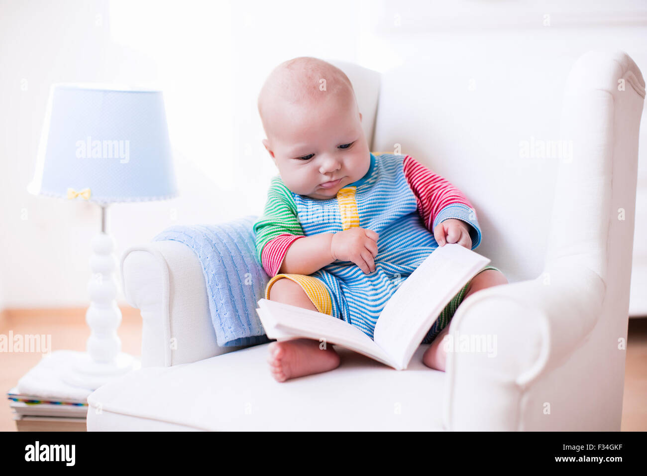 Cute funny baby boy reading a book sitting in a white chair at home.  Children read books in a library seat Stock Photo - Alamy