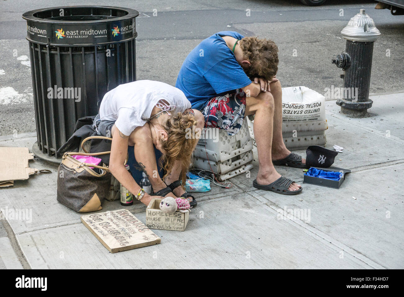 dejected homeless young people couple sit on the sidewalk in midtown Manhattan begging for spare change with heads lowered Stock Photo