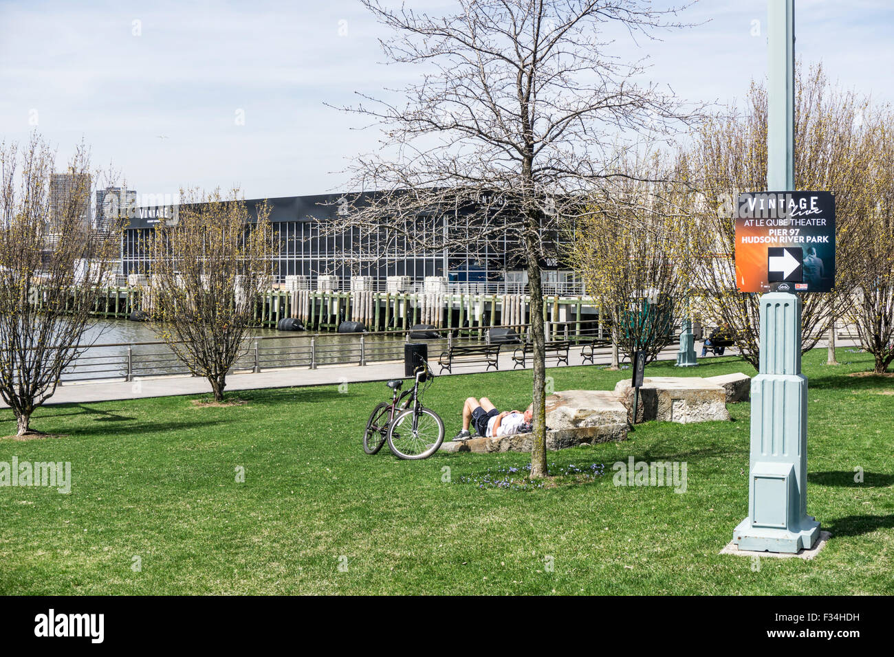 peaceful afternoon Hudson River park with resting bicyclist forsythia coming into bloom view of water & new theater on Pier 97 Stock Photo