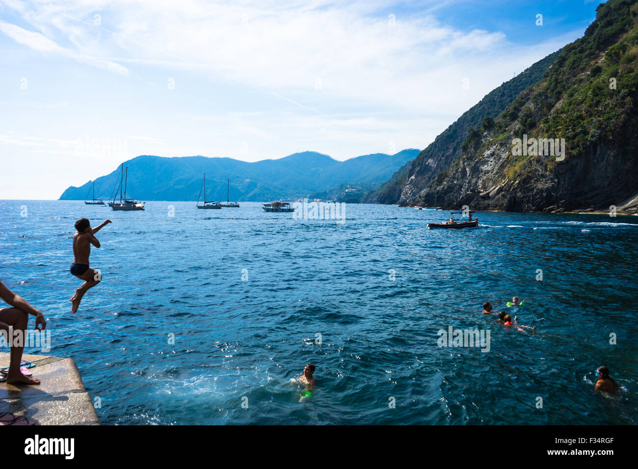 A boy jumps off the dock while friends swim at Vernazza in Italy's CInque Terre. Stock Photo