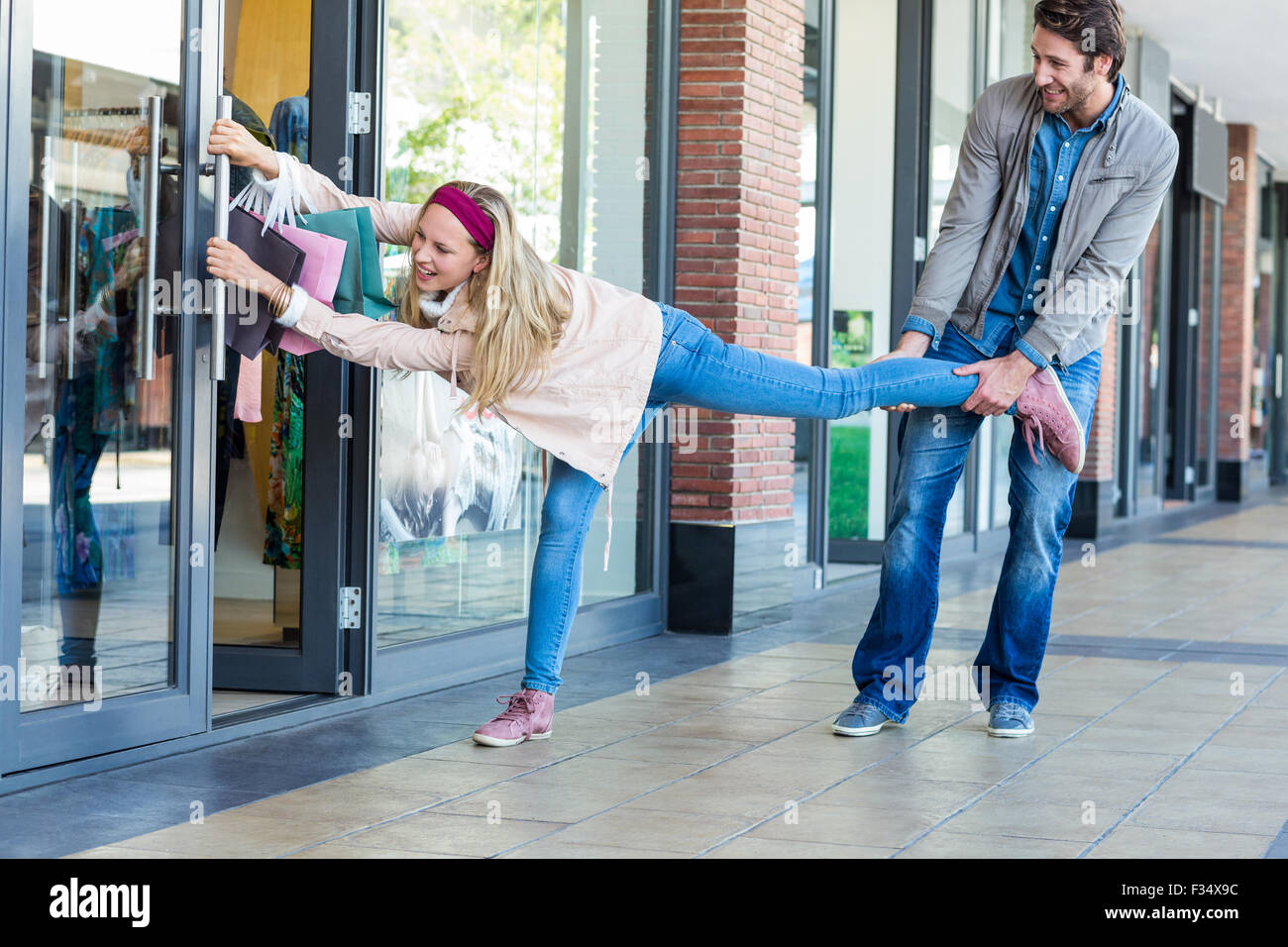 Smiling man trying to pull away his girlfriend from clothes store Stock ...